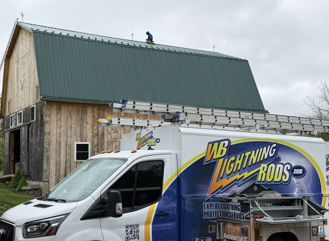 WB Lightning Rods van beside a classic gambrel-roof barn fitted with lightning rods